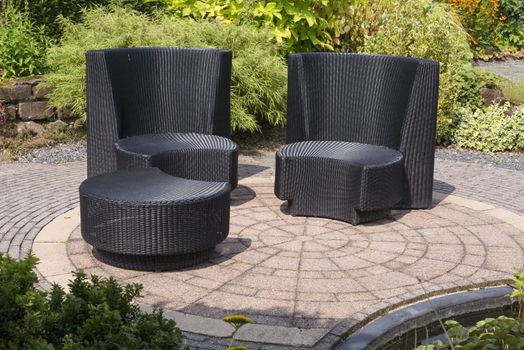teracce with rattan relax chairs in garden with small pond in front and green plants as background