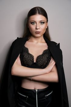 Beautiful young white girl close-up in a black jacket on a gray background. Make-up artist, beauty salon, magazine. Arms crossed. Vertical portrait.