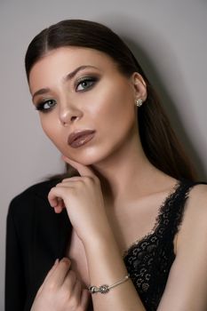 Beautiful young white girl close-up in a black jacket on a gray background. Make-up artist, beauty salon, stylist, magazine