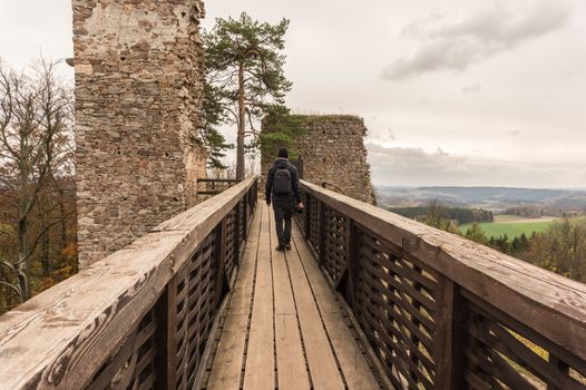 Man tourist photographer holding camera walking on old wooden bridge in autumn.