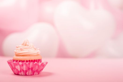 Valentine day love cupcake decorated with cream on pink and white party heart balloons background with copy space for text