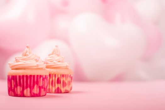 Valentine day two love cupcakes decorated with cream on pink and white party heart balloons background with copy space for text