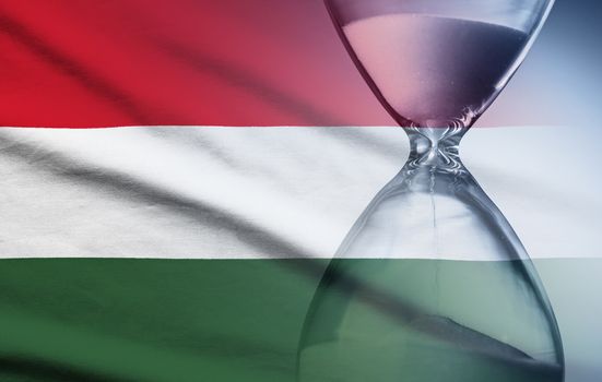 Hourglass with running sand over the flag of the Hungary in a concept of urgency, countdown , deadlines and time management