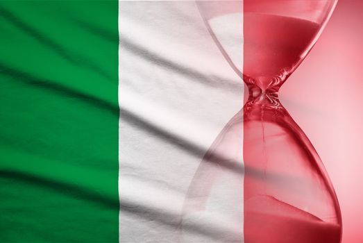 Hourglass with running sand over the flag of the Italy in a concept of urgency, countdown , deadlines and time management