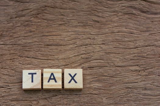 Tax with wooden alphabet blocks, on plank wooden background with copy space
