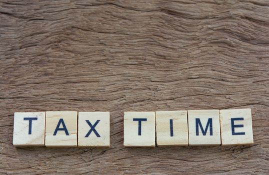 Tax time with wooden alphabet blocks, on plank wooden background with copy space
