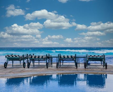 Four chaise lounges on a deck between the pool and the ocean