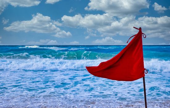 A red warning sign on a beach in front of stormy seas