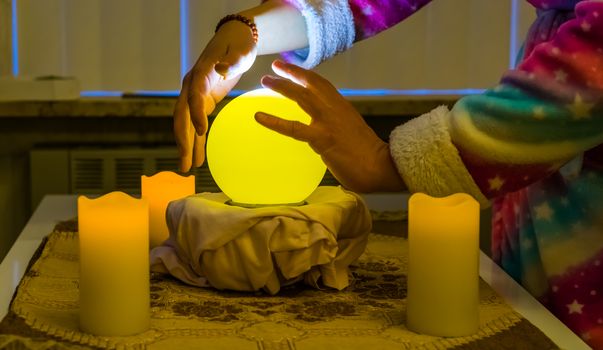 person moving hands around a lighted fortune teller sphere, traditional globe for spirituality and witchcraft