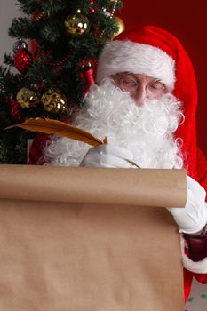 Santa Claus sitting at home and writing on old paper roll to do list with quill pen and ink