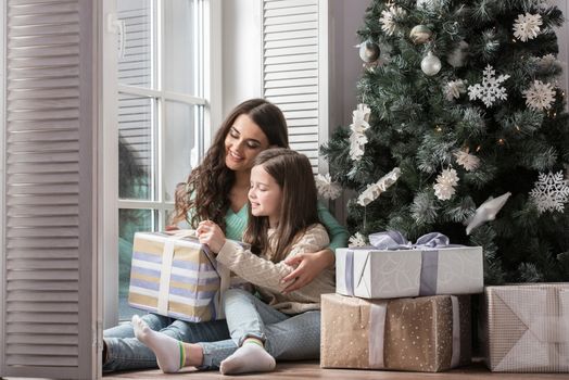 Mother and daughter unwrapping a gift sitting on the floor near christmas tree