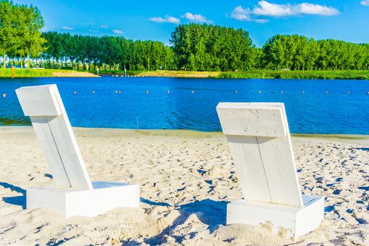 two white beach chairs on the beach in a water landscape with lake view