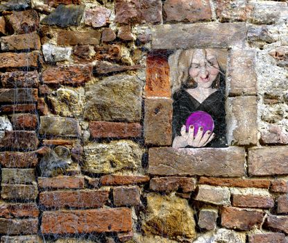 Halloween scary witch holding a glass sphere window peek through a brick wall full of spider webs