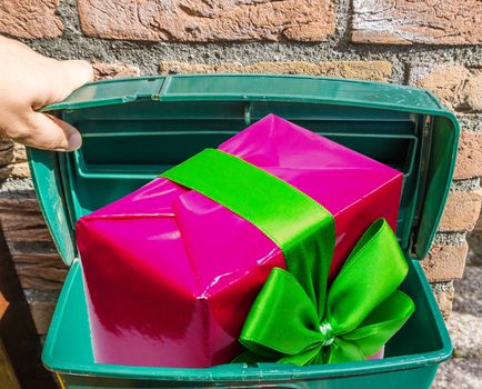 Big pink Christmas present with ribbon in a classic green mailbox