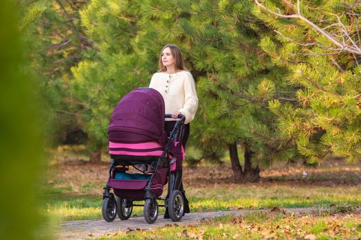 Mom walks with newborn baby in autumn city park