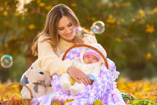 Mom happily looks at the two-month-old baby sleeping in a basket, flying soap bubbles