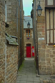 Narrow passage between two traditional stone buildings with red entrance door ahead