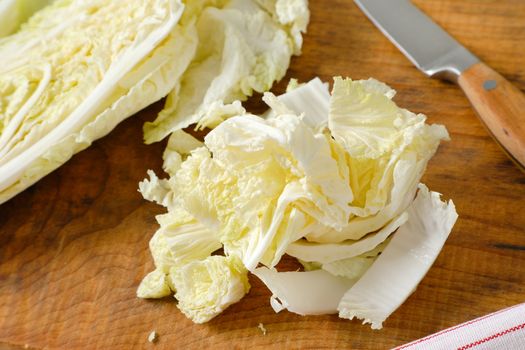 Chinese cabbage leaves and kitchen knife on wooden cutting board