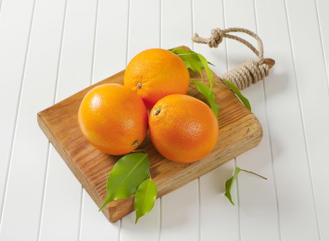 Three whole ripe oranges and leaves on cutting board