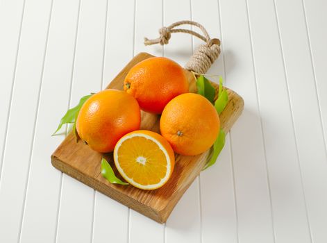 Three whole ripe oranges and a half on cutting board