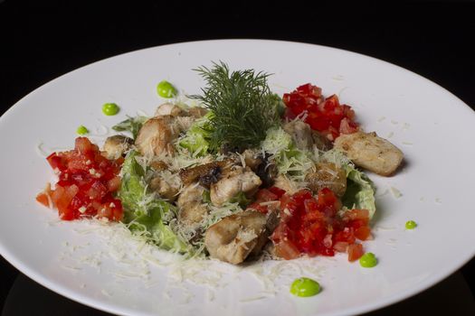 On a white plate salad of meat, tomatoes, lettuce, dill, sprinkled with cheese, on a black background.Fried meat with vegetables.