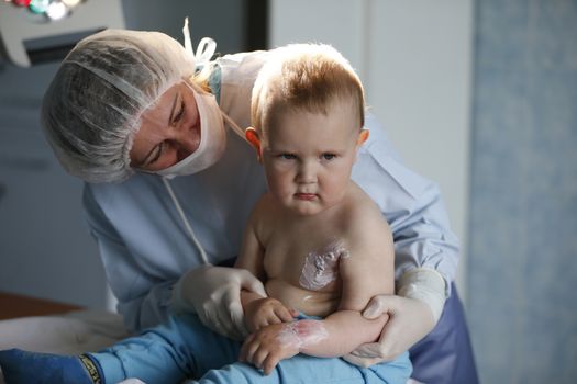 To a little boy, a nurse heals a burn.Kid in the hospital wounded.The doctor heals a little bit.The boy was burned.Little hospital patient