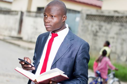 Young businessman with an open book in his left hand and manipulating a portable phone in his right hand
