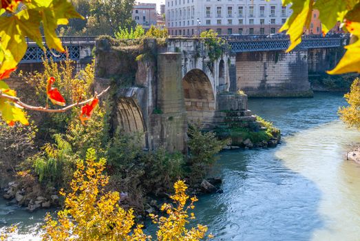 The remains of the ancient Ponte Rotto or Pons Aemilius Broken Bridge with Isola Tiberina Tevere Island in the background, Roma, Italy
