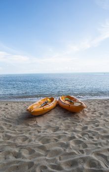 Two colorful orange kayaks on a sandy beach ready for paddlers in sunny day. Several orange recreational boats on the sand. Active tourism and water recreation