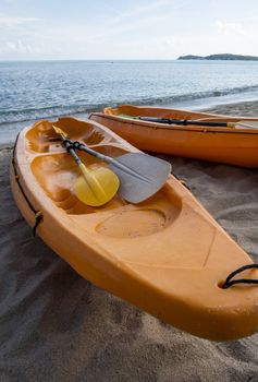 Two colorful orange kayaks on a sandy beach ready for paddlers in sunny day. Several orange recreational boats on the sand. Active tourism and water recreation