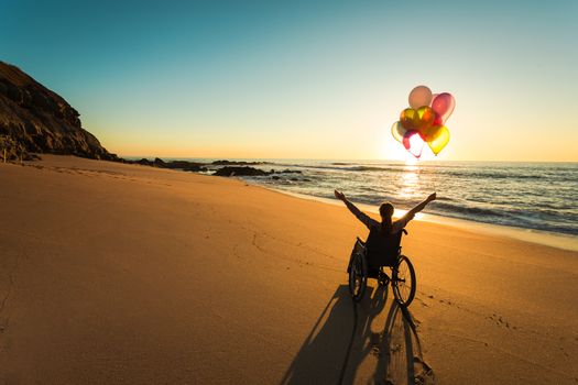 Handicapped woman on a wheelchair with colored balloons at the beach