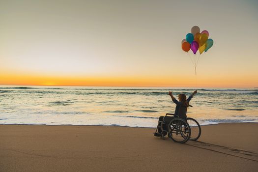 Handicapped man on a wheelchair with colored balloons at the beach
