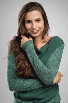 Beautiful woman standing over a gray background with her hand on the hair and smiling