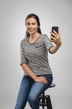 Beautiful happy young woman sitting on a bench and makign a selfie