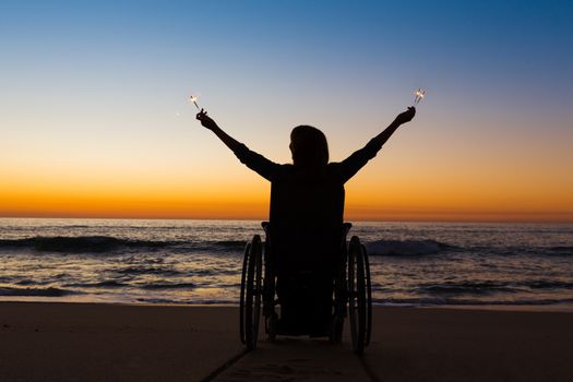 Handicapped woman in a wheelchair holding fire sparklers on the beach