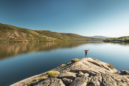 Shot of a man hiking near a beautiful lake with arsm raised