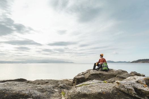 Man with backpack and sitting on the rocks while enjoying the beautiful morning on the beach