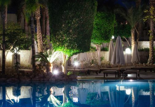 blue water pool and green palm trees with street lamps at night without people in sharm el sheikh egypt