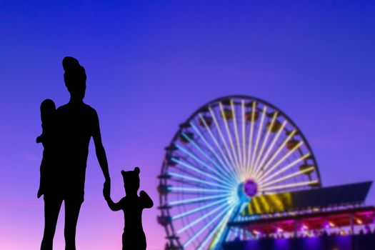 Family silhouette in a theme park looking at the ferris wheel mother with her little daughter and baby