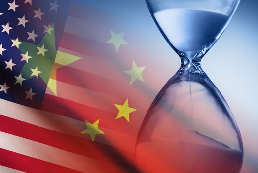 Hourglass with running sand measuring passing time over the flags of America and China in a deadline concept