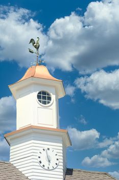 A clock and a weathervane on a cupola against blue sky