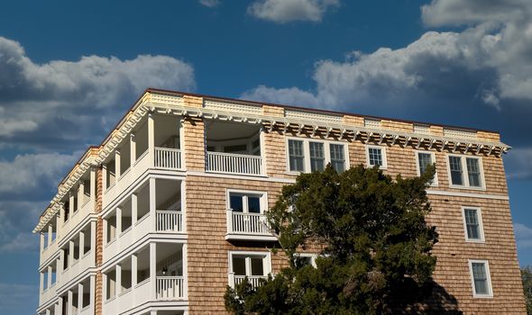 A large wood shingled beach house with balconies and a tree against a blue sky