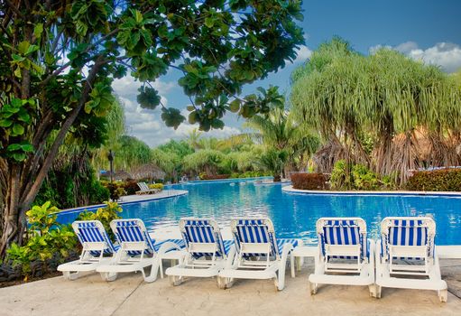 A nice tropical pool with blue striped chairs