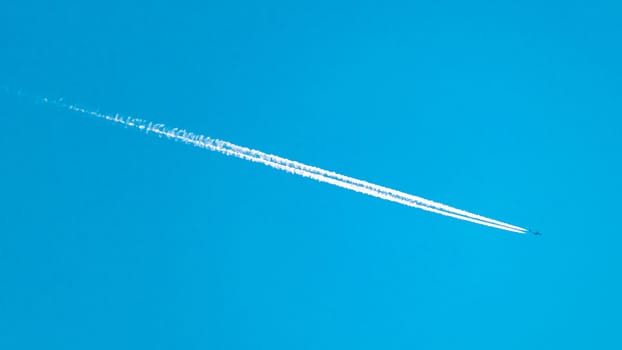 An airplane flies high overhead, leaving a white vapor trail streaking across the blue sky behind it.