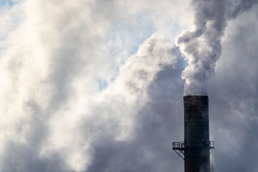 Thick white smoke and steam billows out of a smokestack at an industrial textile factory, filling the sky with thick clouds on a cold winter day.