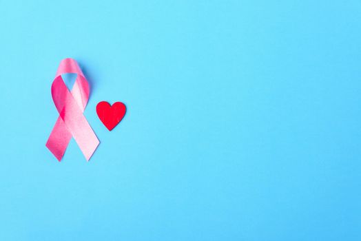 Breast cancer month concept, flat lay top view, pink ribbon and red Heart on blue background with copy space for your text