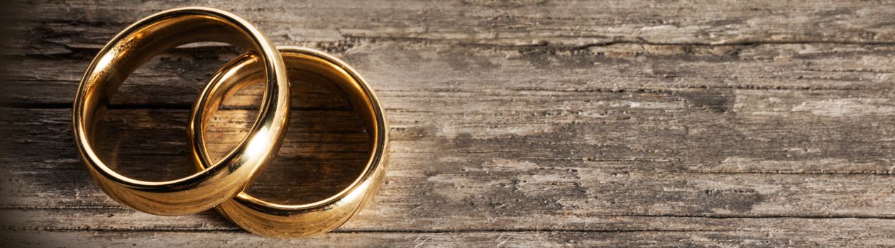 Two golden wedding rings on wooden background with copy space for text