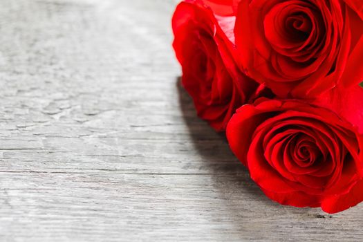 Three red roses on wooden background with copy space