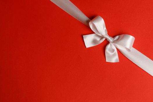 White satin ribbon bow on red paper background