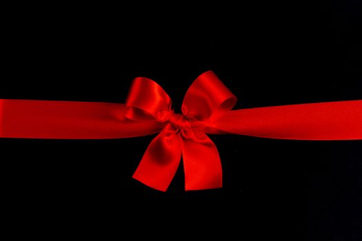 Red satin ribbon bow on black paper background